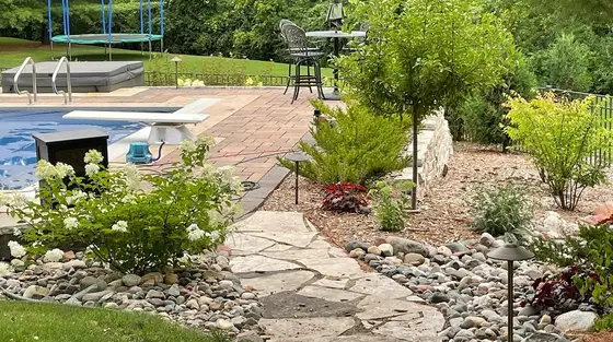 Backyard pool surrounded by a flagstone patio, river-rock beds and layered shrub plantings