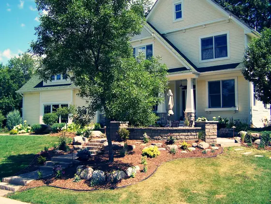Front-yard landscaping with a mulched planting bed, natural stone steps, and boulder edging beneath a shade tree