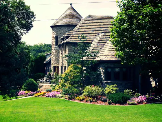 Stone home framed by a manicured lawn and colorful flowering foundation beds