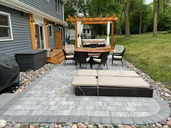 Backyard paver patio with a cedar pergola, hot tub and dining set edged with river rock