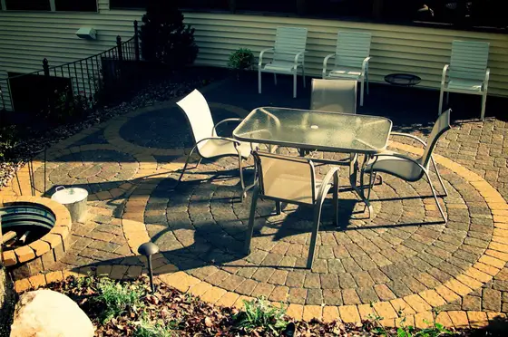 Circular brick paver patio with a glass-top dining set and chairs beside a home