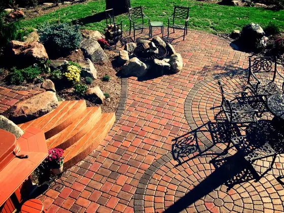 Circular brick paver patio with a central fire pit, curved wood deck steps and wrought-iron furniture