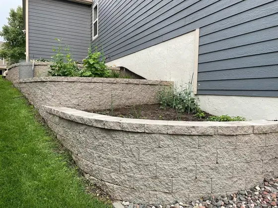 Curved tiered block retaining wall forming a raised garden bed alongside a home