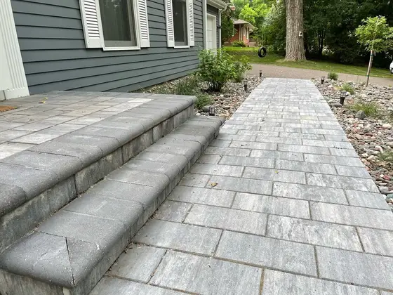 Paver walkway and matching front steps bordered by a river-rock planting bed