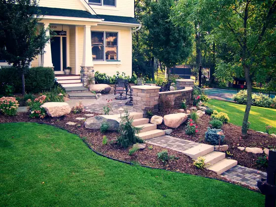 Paver steps and seat wall leading to a front patio framed by boulders and layered flower beds
